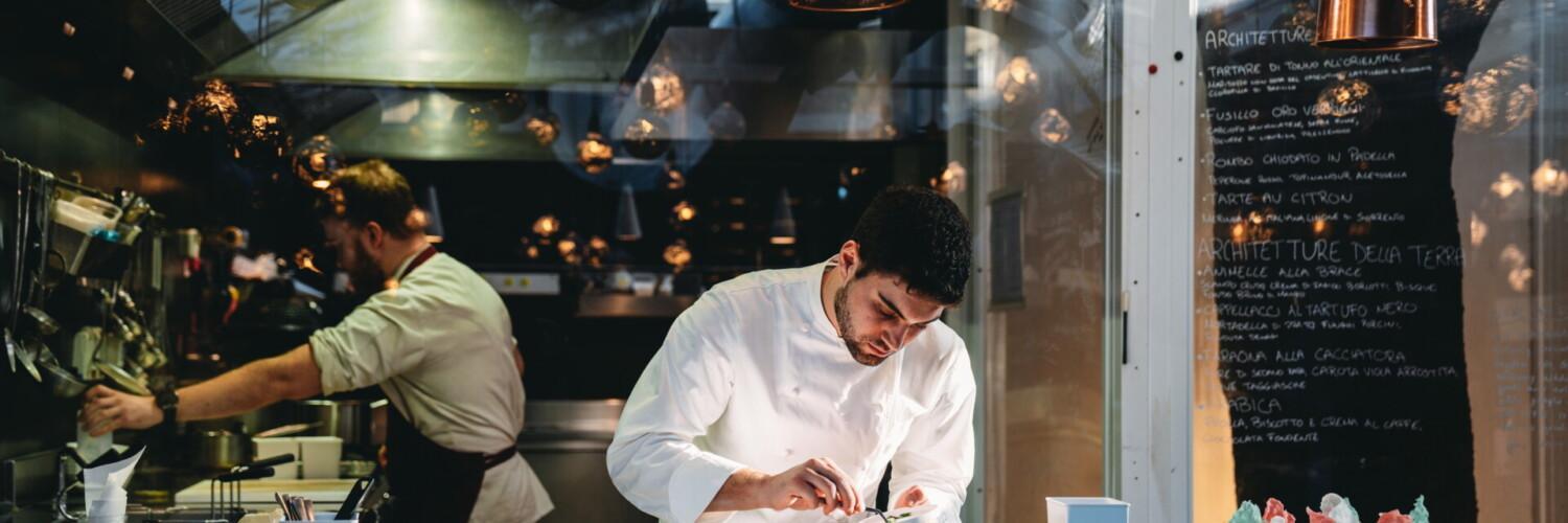 Kockar i arbete i ett professionellt restaurangkök med rostfria arbetsytor och öppet kök.