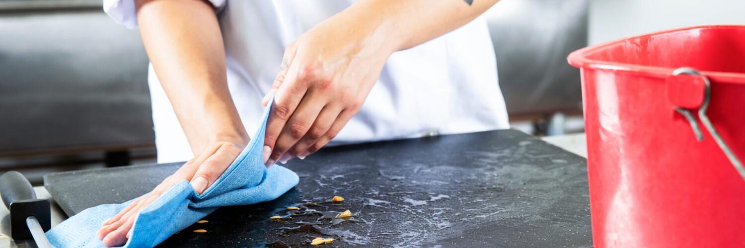 Kockhand rengör skärbräda med blå mikrofiberduk i professionellt kök.